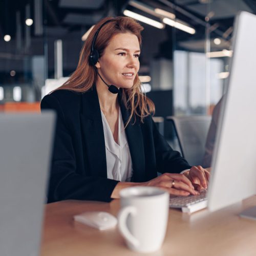 bella-donna-d-affari-cuffia-che-lavora-al-computer-mentre-e-seduto-un-ufficio-moderno